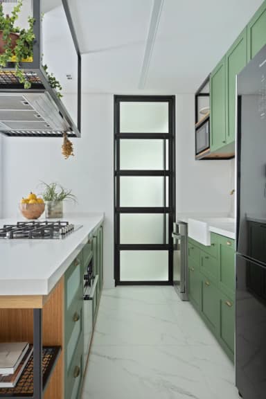 Cozinha com armários verdes, bancada clara e porta de vidro com perfil preto