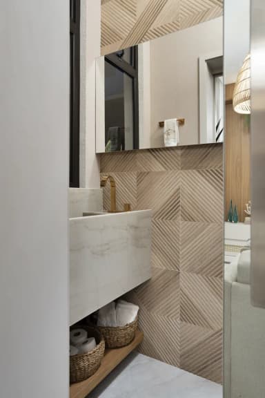 Lavabo com bancada de mármore, torneira dourada e revestimento geométrico
